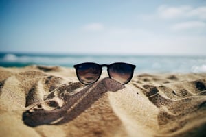 A pair of sunglasses on a beach in summer.
