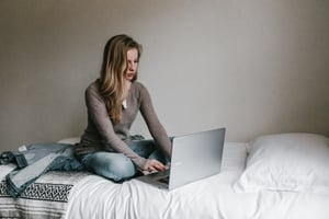 A woman on a computer on her bed at home.